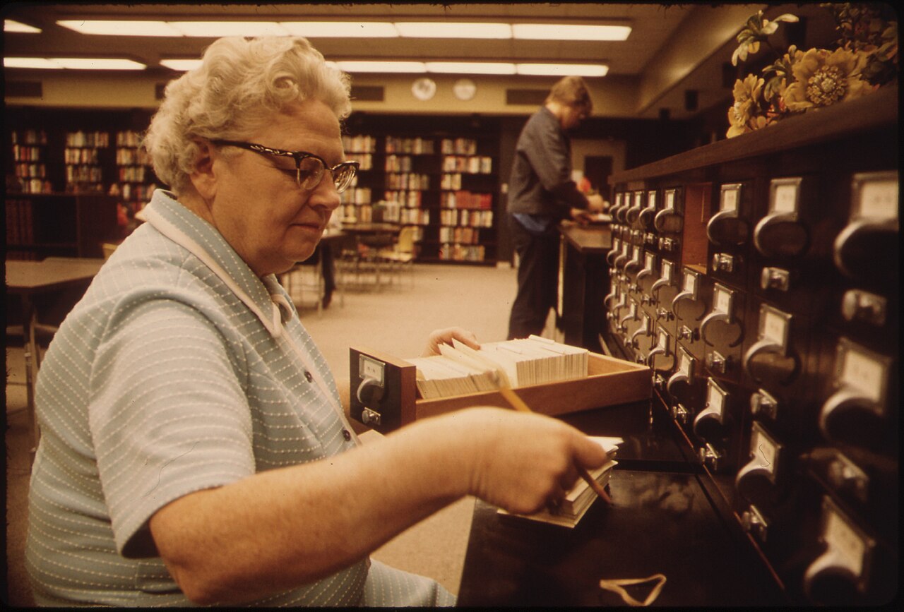 Librarian standing at wooden card-catalog drawers in a Minnesota high-school library, October 1974